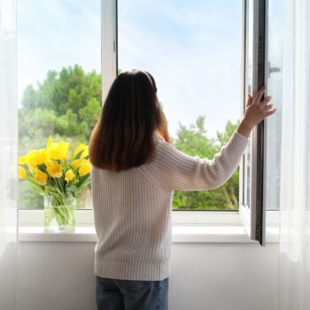 woman opening and looking out her window next to a vase of tulips